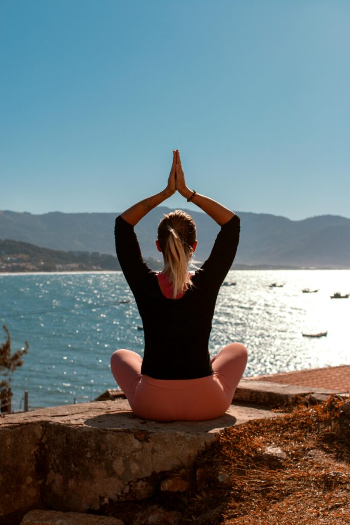 Woman practicing yoga by the sea at sunrise, embracing a healthy lifestyle.
